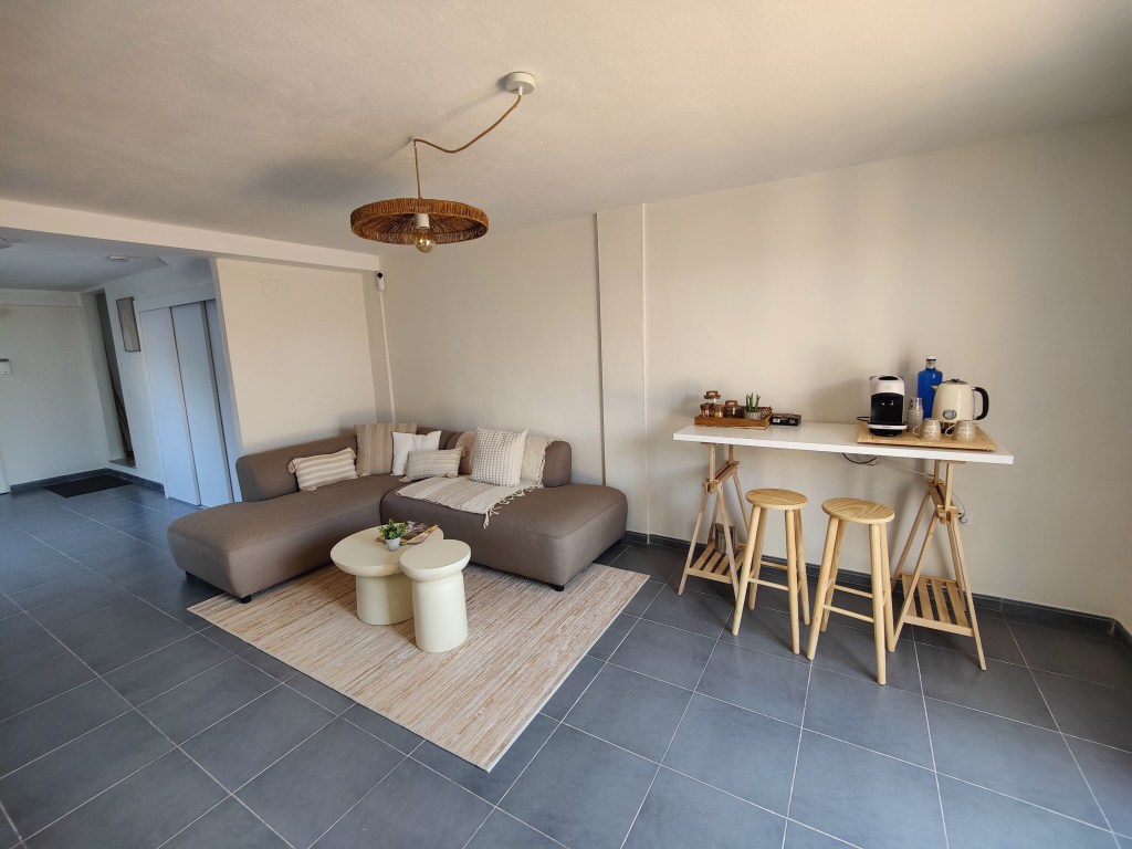 The living room in the image features a couch, small tables, and kitchen necessities. A brown, L-shaped sofa beckons with ...